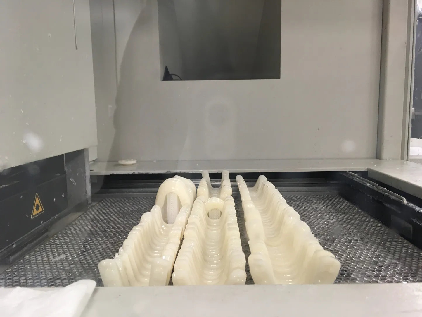 Rows of batched splints standing inside the stereolithography printer, photographed through the machine glass.